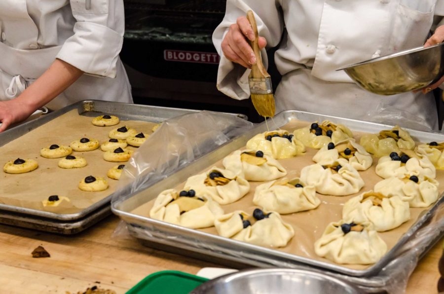 A baking student brushes eggwash onto blueberry gallettes.