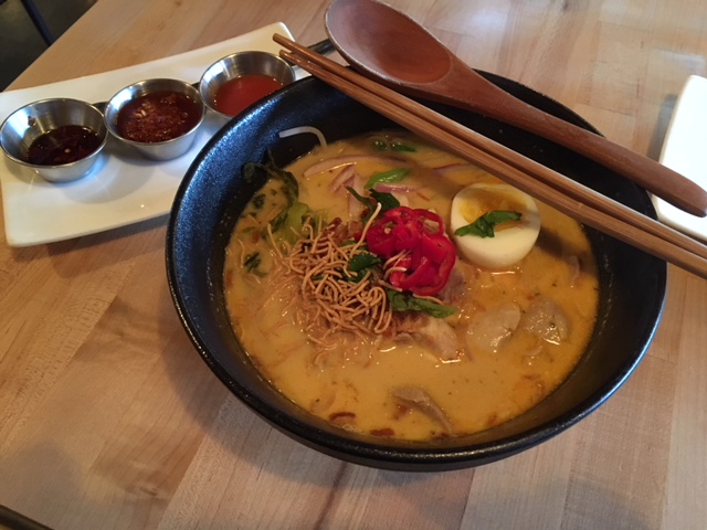 The orange chicken curry noodle soup bowl served with savory sauces.