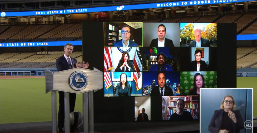 Governor Gavin Newsom stands at a podium in Dodger Stadium in Los Angeles. A screen behind him shows multiple public officials and an ASL interpreter is shown on the bottom right.