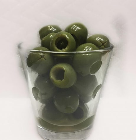 A photo of a shot glass filled with green olives.