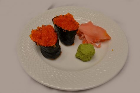 A photo of two pieces of tobiko (fish egg) nigiri with fresh ginger and wasabi.