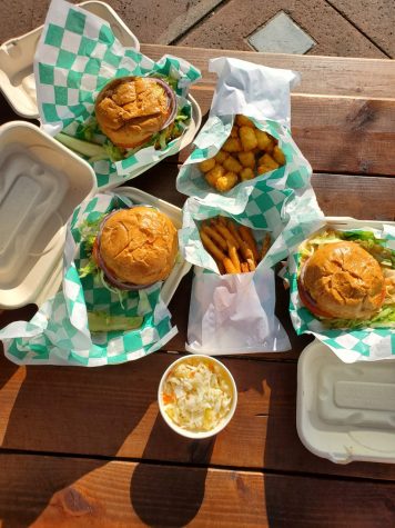 A picture of plant-based burgers wrapped in green and white paper; pictured with a side of french fries, tater tots and pineapple coleslaw.