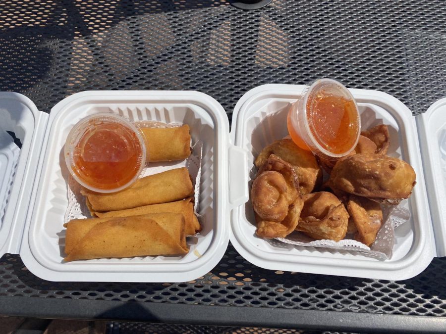 Two white takeout containers holding crispy fried eggs rolls and cheese puffs, served with two small plastic cups of sweet and sour sauce.