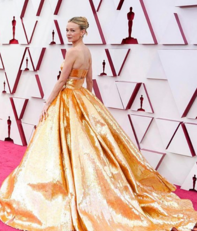 Actress Carey Mulligan in a top-fitted gold Valentino gown with a full skirt on the red carpet.