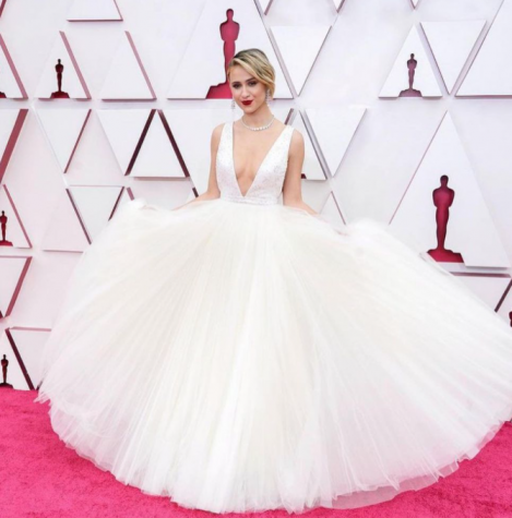 Maria Bakalova holds out her pure white tulle dress. The top is sleeveless with a plunging neckline.