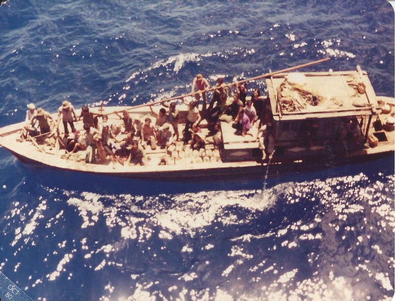 A photograph of a wooden boat at sea, carrying dozens of Vietnamese refugees.