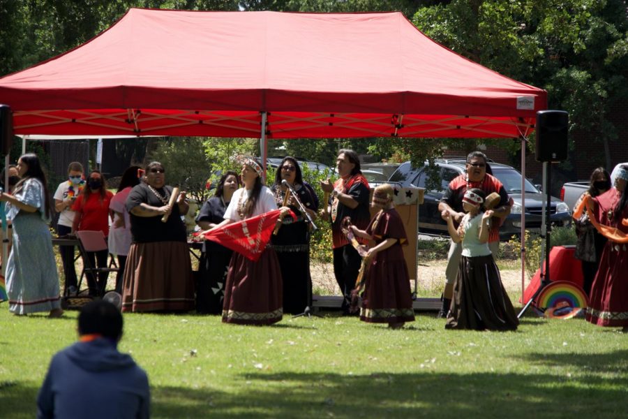 A picture of a group of Pomo dancers performing under a read canopy.