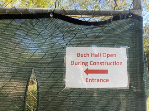 A laminated sign posted on a construction fence points students to the entrance of a building.