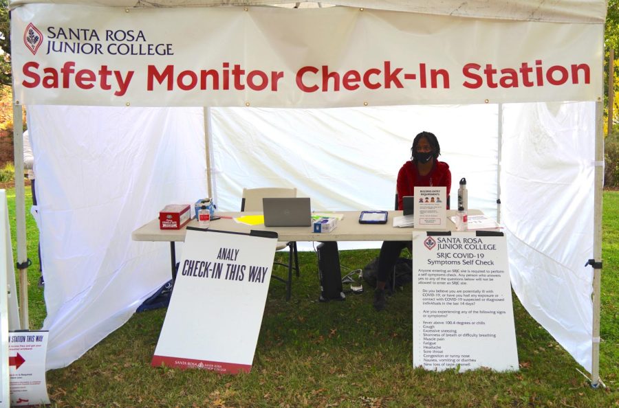 A woman sits behind a safety monitor check-in station in a white tent