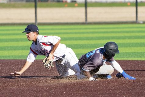 A baseball player slides onto a plate as a player on the other team attempts to stop the play.