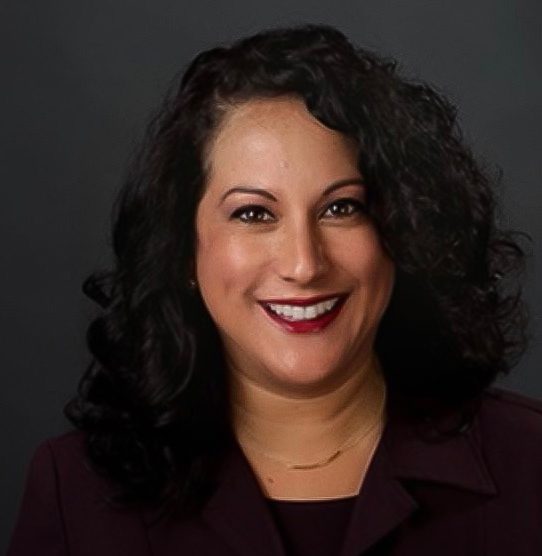 Former SRJC Student Support Manager Hilleary Zarates smiling headshot on a dark grey background.