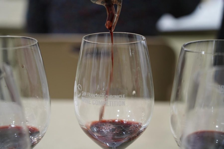 Three wine glasses filled with tasting portions of red wine. The middle glass is being poured into.