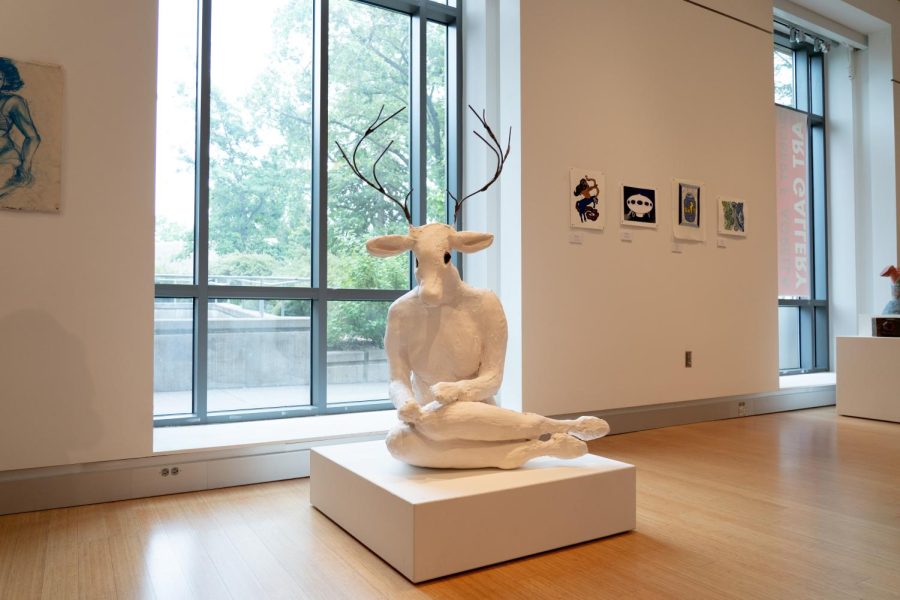 A white sculpture depicting a humanoid deer rests near the window of the art gallery.
