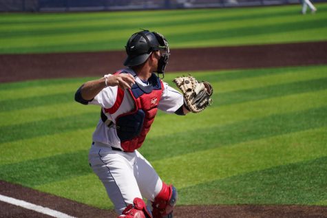 A catcher winds up to throw a baseball on a grassy baseball field.