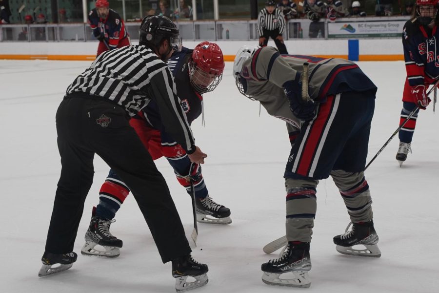 A skater from Santa Rosa Junior College and Gonzaga University face off against each other,wait for a referee to drop a puck to resume play.