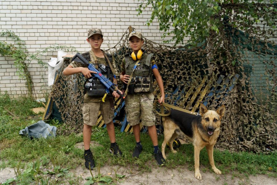 Two children and their dog station a mock checkpoint on Aug. 10, 2022 on a road into Malaya Rohan, Ukraine, a town outside Kharkiv that came under Russian shelling. 