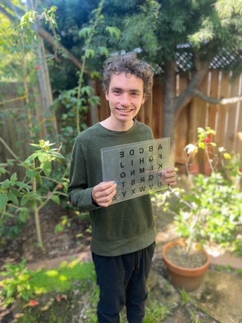 SRJC student Noah McSweeney writes by using a letterboard with letters that he can point at to spell words his communication partner can write down. Using this format in his SRJC writing classes, McSweeney has learned to write long, in-depth essays and now collaborates with other “spellers” to write songs and poetry. 