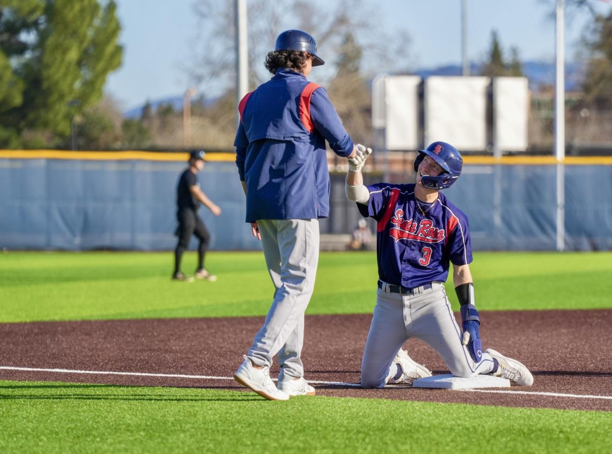 Shortstop Aidan Lombardi fist-bumps third base coach Jeff Bart after diving safely into third in a 4-2 win against Cabrillo College at Santa Rosa’s Cook Sypher Field on Feb. 22, 2024.