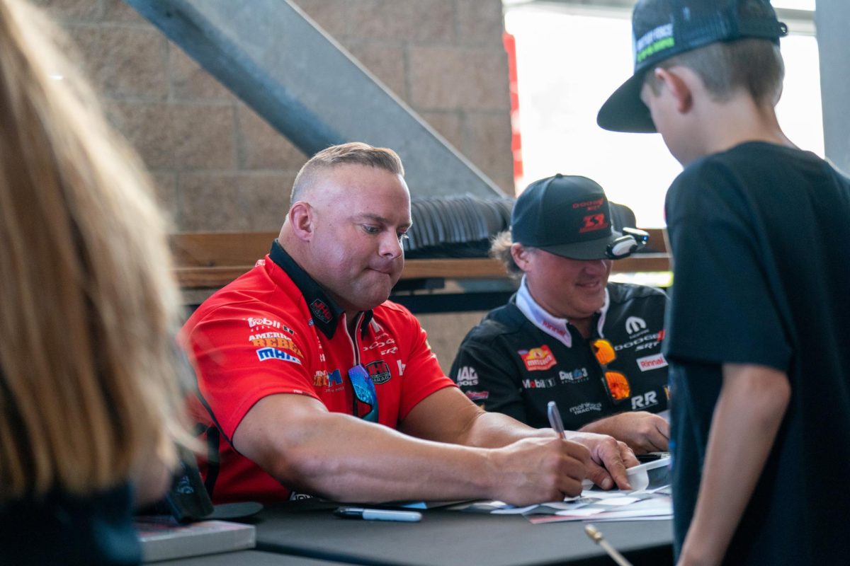 NHRA Funny Car driver Matt Hagan signs autographs for kids alongside Funny Car driver Tony Stewart at the DENSO NHRA Sonoma Nationals on Friday, July 26, 2024 in Sonoma.