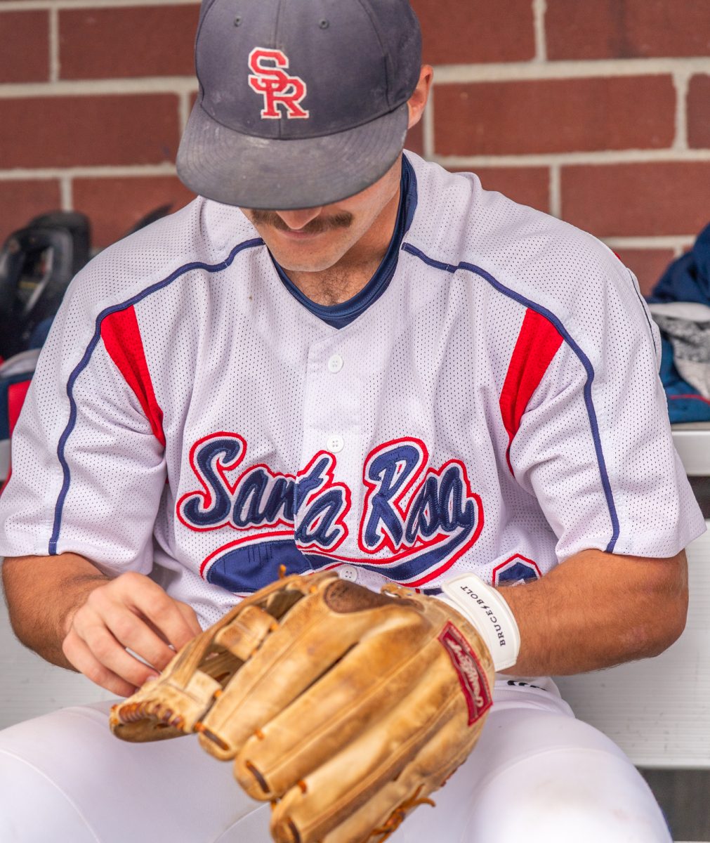 Freshman center/left fielder Shane Moran adjusts the laces of his glove in the dugout ahead of the game against Lassen College at home, Sunday, Feb. 16, 2025.