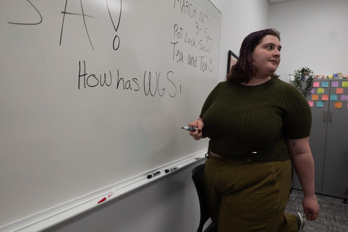Madelyn Boyd writes on a whiteboard inside of the Women and Gender Studies club room located in 3118 Stevenson at Sonoma State University on April, 2, 2025. The text is part of a prompt for a series of short interviews for the WGS club's instagram.