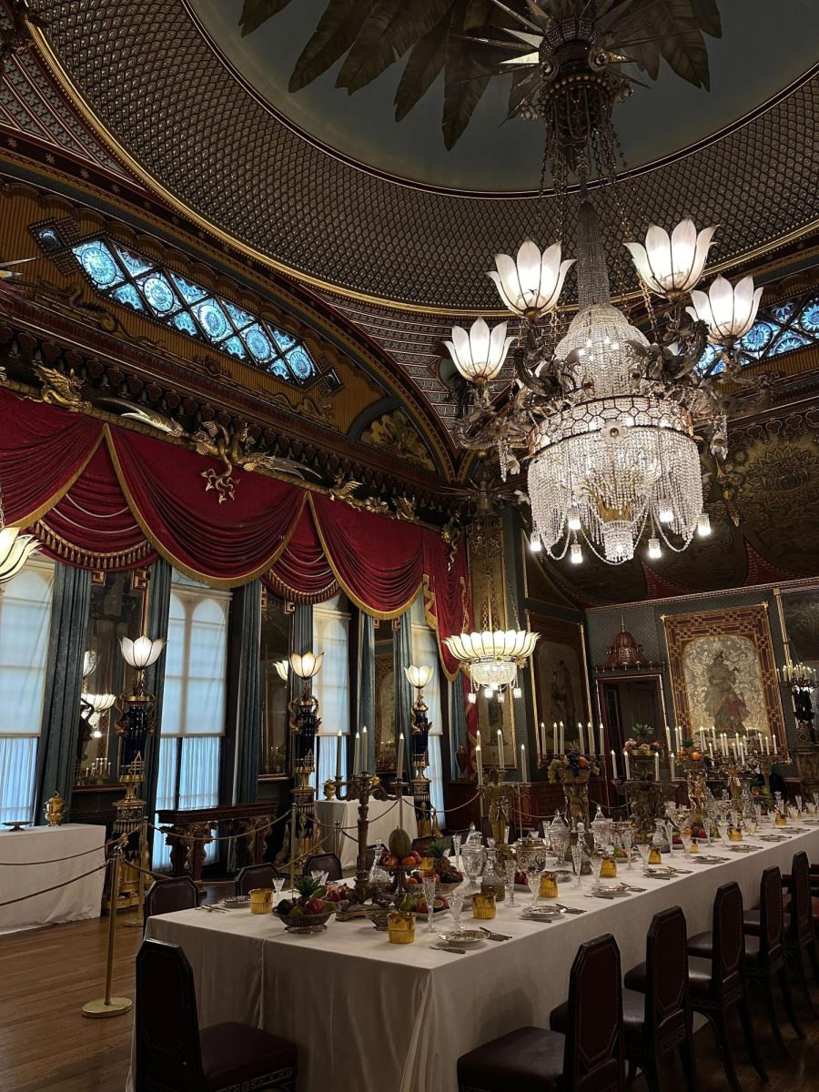 The Banqueting Room of the Royal Pavillion in Brighton, England is blanketed in baroque decoration, with velvet curtains and gilded ornaments framing the well-kept space.