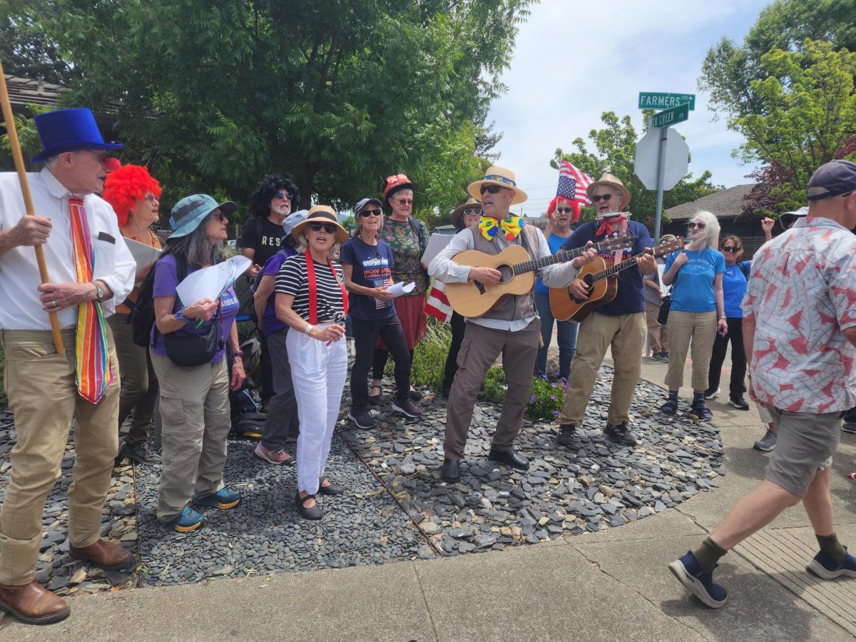 Protestors sing at the corner of Rock Creek and Farmers Lane as the No Kings No Clowns parade marches by.