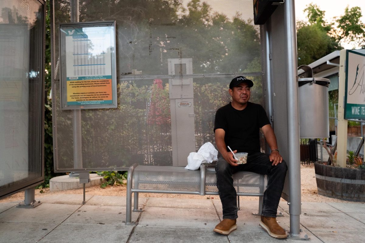 Alfonso Angeles sits at a bus stop eating ceviche at 6:51 p.m. on Thursday, Aug. 21, 2025. Angeles' primary worry is the overall temperature but believes that Cal Fire firefighters are capable of keeping the situation under control; he mentions that this is something he's accustomed to seeing every year.