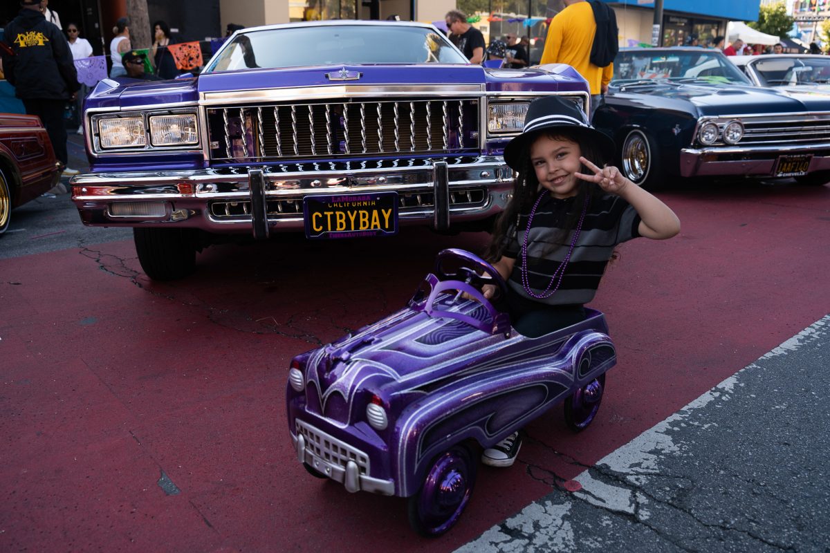 A child poses in a pedal car in front of a lowrider painted by the same artist, during the King of the Streets lowrider parade on Mission Street in San Francisco on Saturday, Sept. 20, 2025.