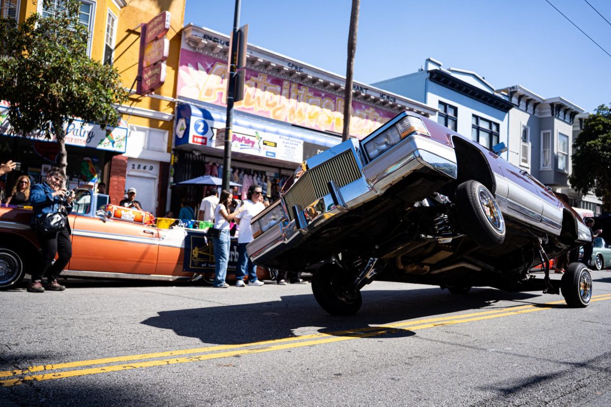 A lowrider cruises down Mission Street with one wheel raised during the King of the Streets lowrider parade in San Francisco on Saturday, Sept. 20, 2025.