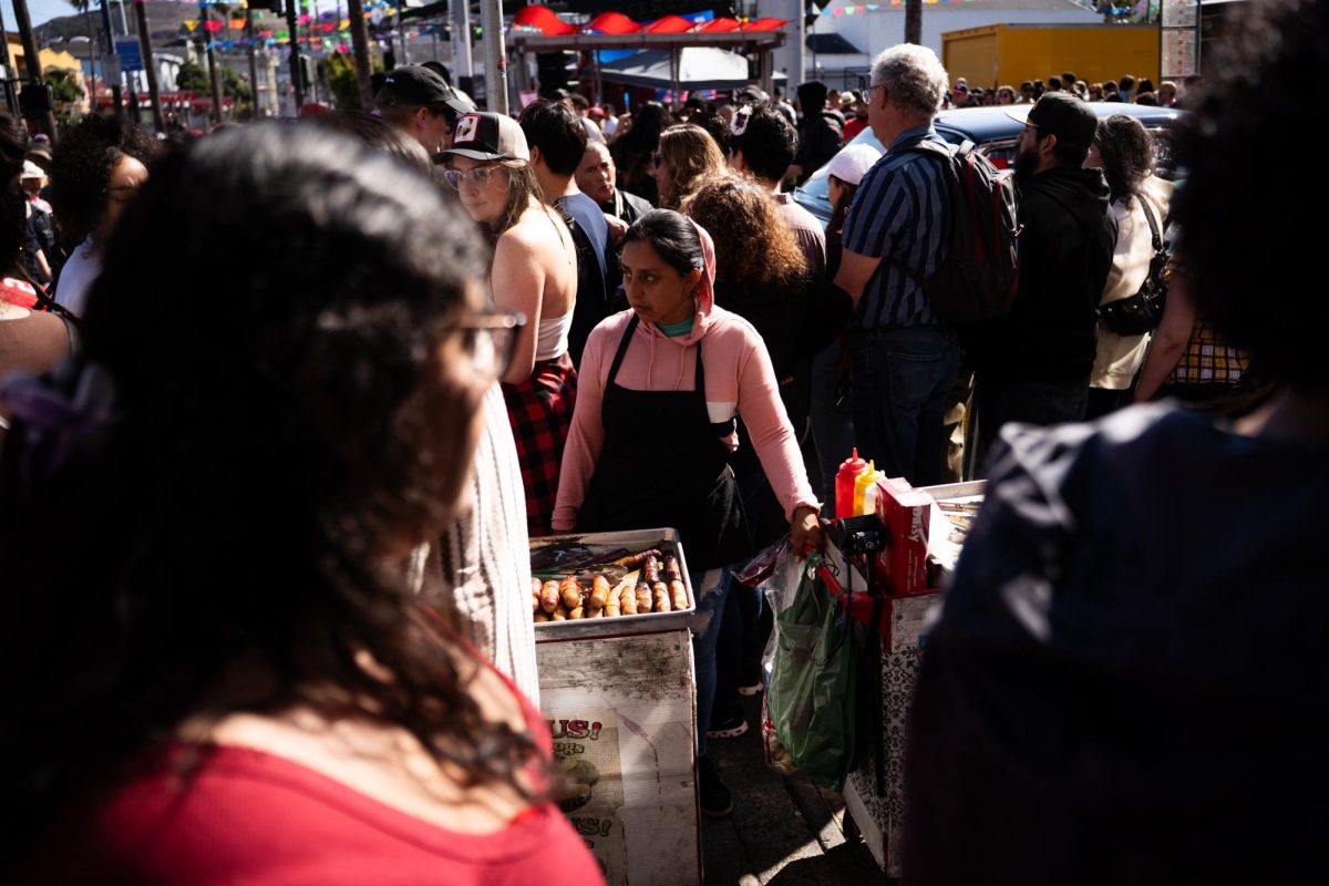 A hot dog vendor gets surrounded by a crowd as people gather for the Thrill of the Hop contest during the King of the Streets lowrider parade on 24th and Mission Street in San Francisco on Saturday, Sept. 20, 2025.