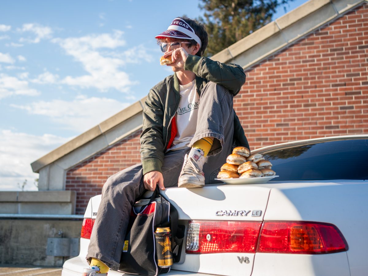 Oak Leaf reporter Archibald Henderson sits on top of their Camry, White Castle burger in hand while recounting a wild White Castle experience this past summer on Thursday, Sept. 11 in the SRJC parking garage.
