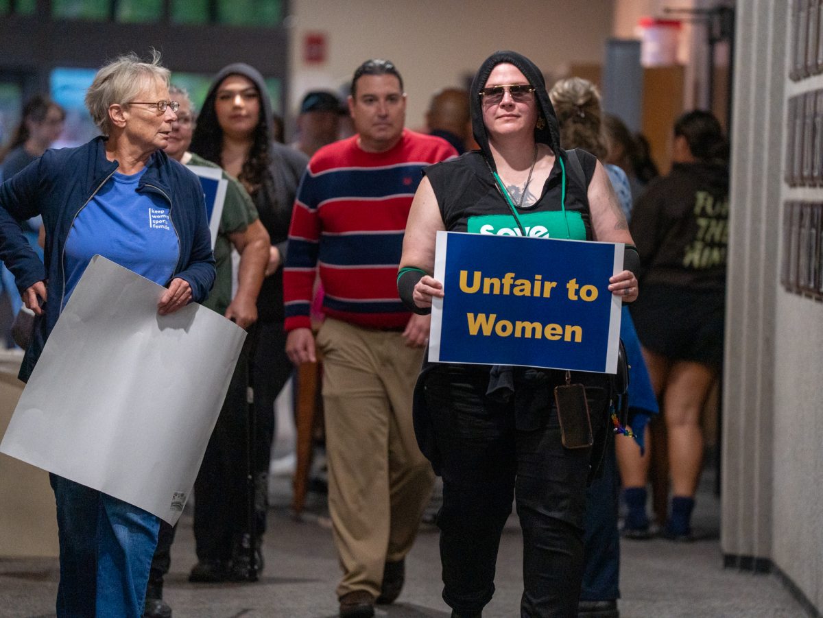 An community member opposed of a trans athlete's rights to participate on the SRJC women's volleyball team walks down the hallway to enter the gym holding a sign that says "Unfair to Women" ahead of Wednesday night's matches against American River on Wednesday, Oct. 8.