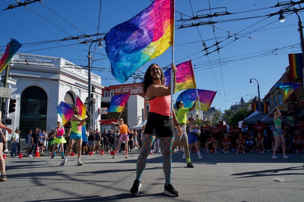 A member of the Harvey Milk Pride Colorguard flashes a smile mid-routine during one of the group’s performances at the Castro Street Fair on Sunday Oct. 5, 2025. The new colorguard group welcomes anyone, regardless of experience, to join them as they march in parades around the Bay Area.  