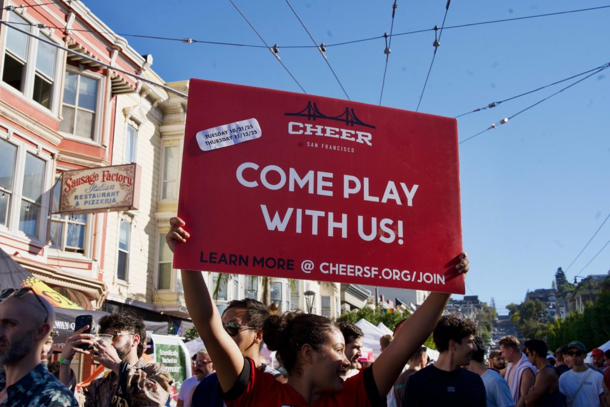 An SF Cheer cheerleader walks through crowded streets holding a sign that promotes the LGBTQ-identified nonprofit organization at the Castro Street Fair on Sunday Oct. 5, 2025.  