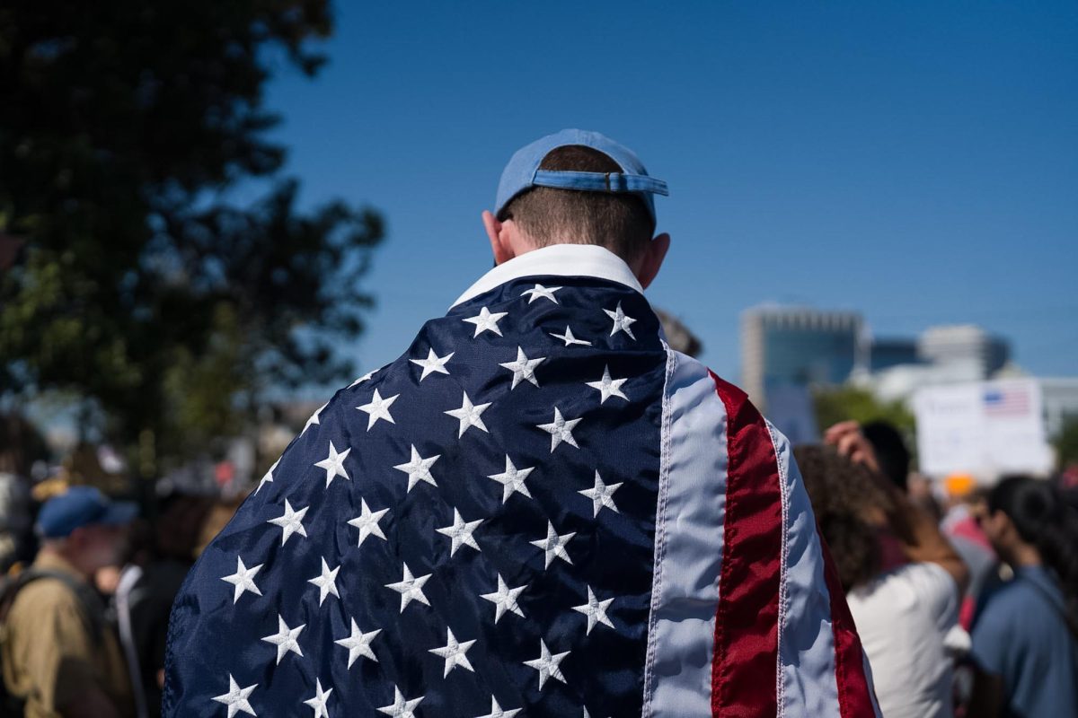 A protestor dons the American flag as a cape while attending a No Kings protest Saturday, Oct. 18, 2025 at Wilma Chan Park in Oakland, Calif. 