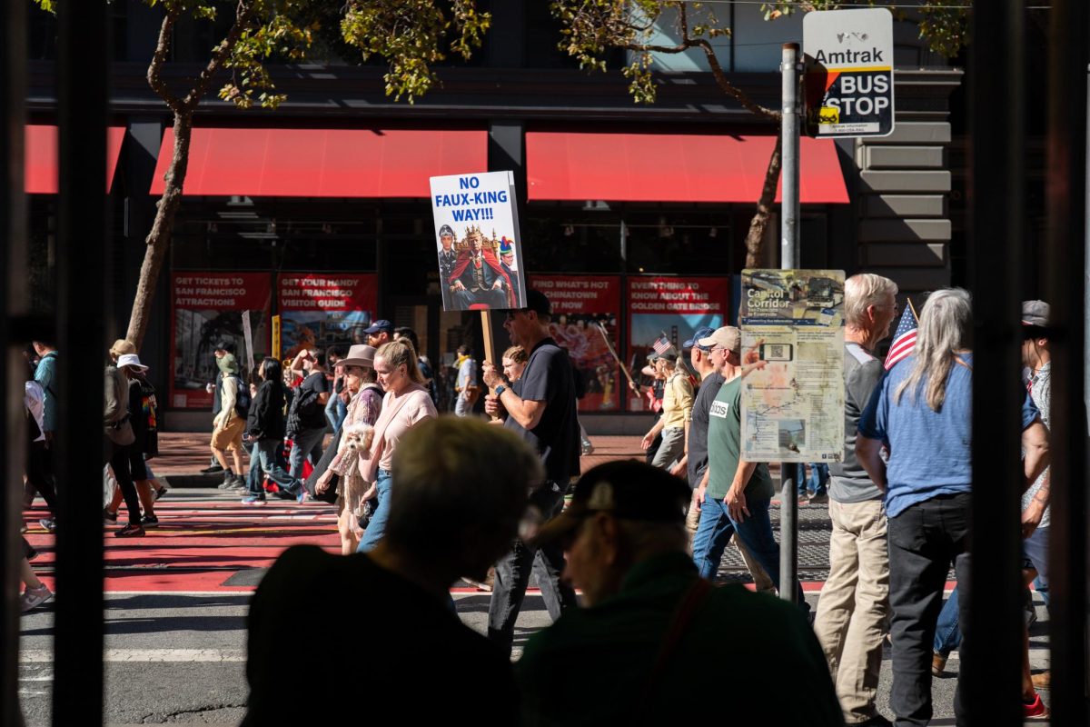 Bystanders watch from the side lines --- like those sitting at a bus stop --- as protestors march down Market Street during the No Kings Protests Saturday, Oct. 19 in San Francisco, Calif.