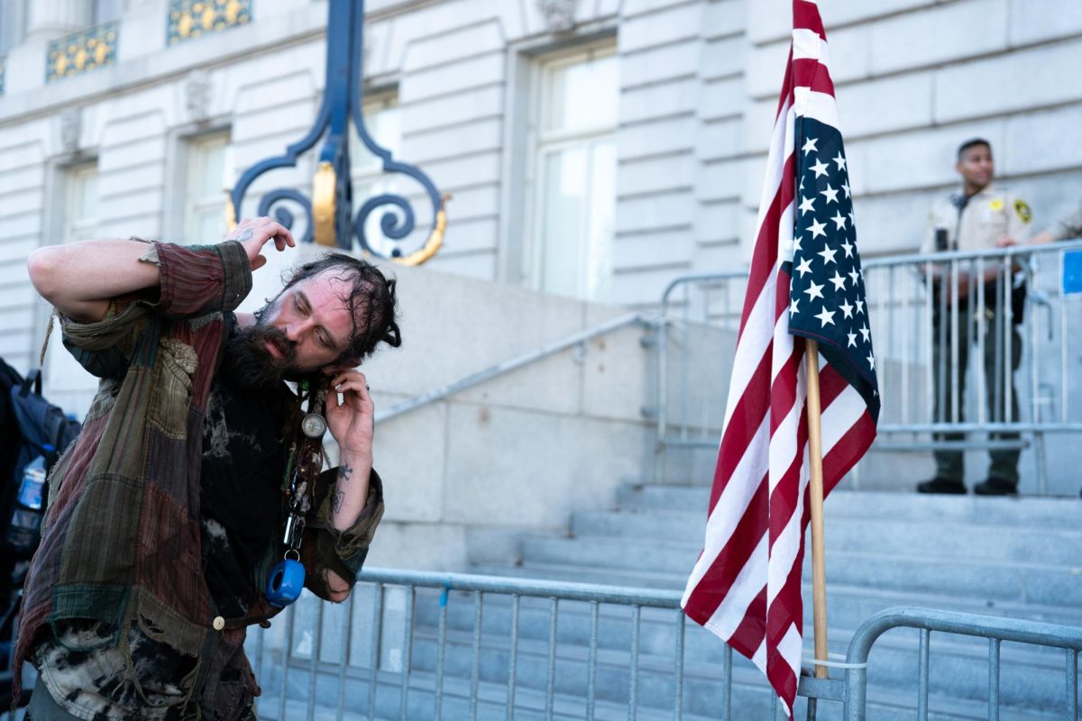 A protestor plants a U.S. flag in front of San Francisco City Hall while "Killing in the Name" by Rage Against the Machine plays off a speaker nearby Saturday, Oct. 19, 2025.