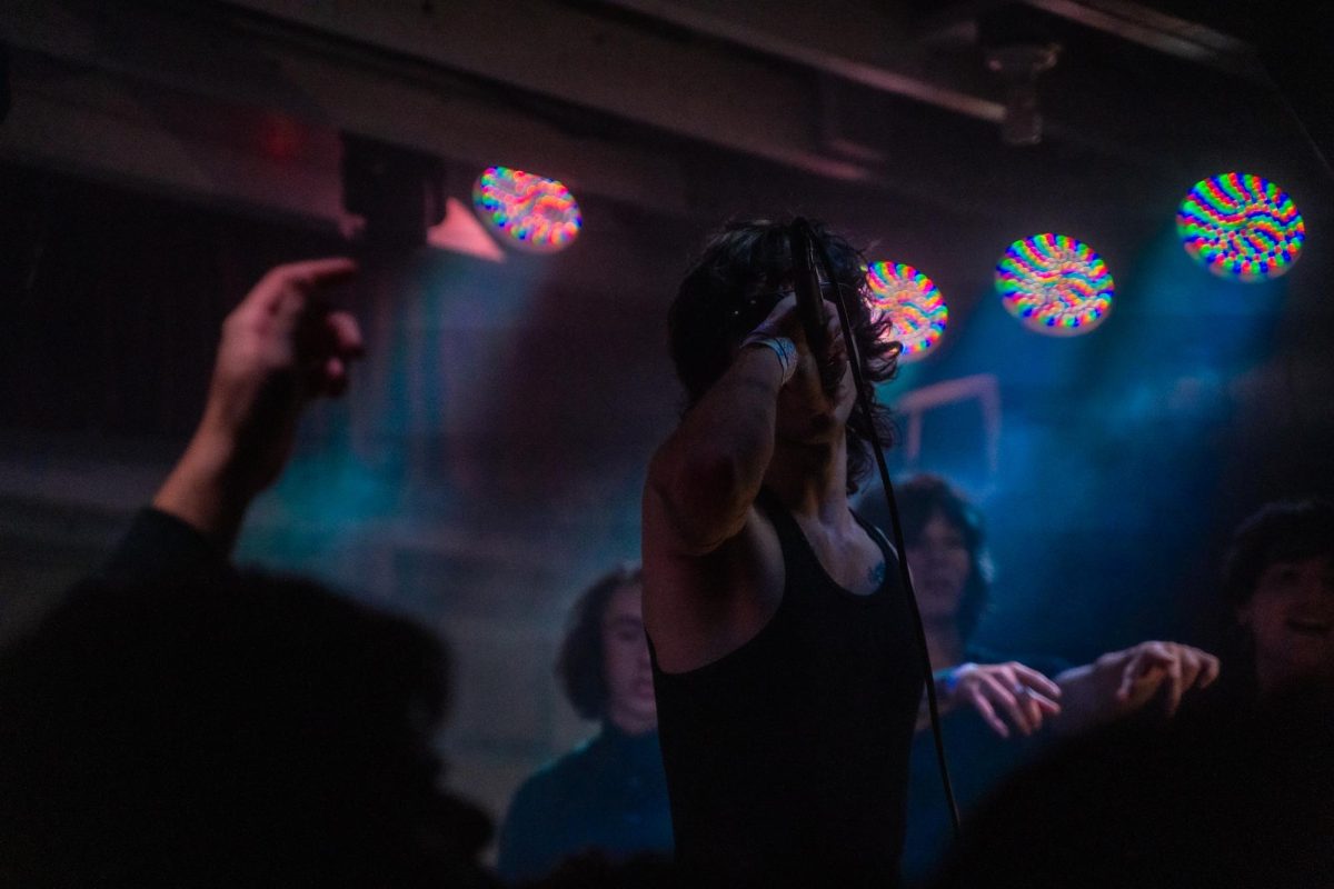 On a folding-table-sized-stage, myspacemark's friends, co-artists and other longtime supporters surround him as he serenades the crowd during his first-ever show Dec. 4, 2025 at the DNA Lounge in San Francisco.