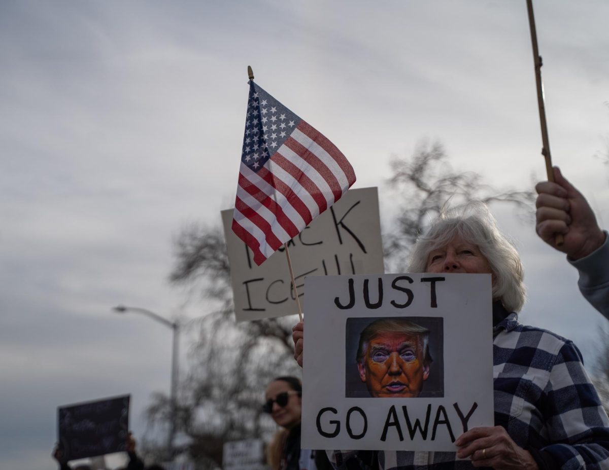 One of hundreds of protestors holds an American flag in one hand and an anti-Trump sign in the other as cars drive past the Free America Walkout on Mendocino Avenue in front of Santa Rosa Junior College Jan. 20, 2026. 