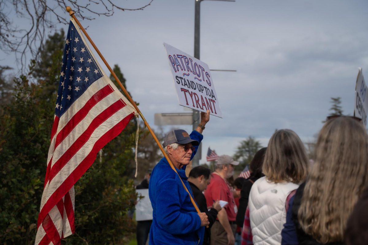 A protestor holds a well-loved American flag in one hand and a red-white-and-blue poster in the other at the Free America Walkout on Mendocino Avenue in front of Santa Rosa Junior College Jan. 20, 2026. 