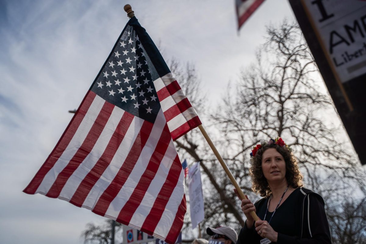 Jessica Melvin, vice president and lead negotiator of the SEIU 1021 Local Chapter at Santa Rosa Junior College is adorned in a flower crown and waves an American flag at oncoming traffic during the Free America Walkout on Mendocino Avenue Jan. 20, 2026.