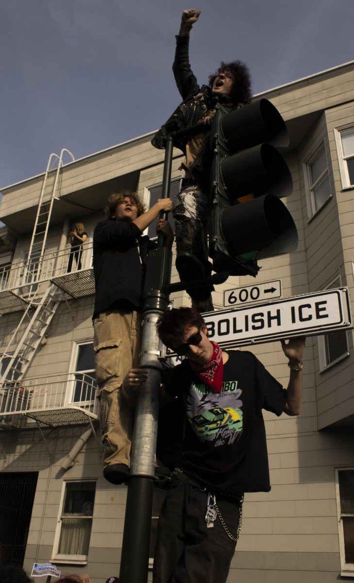 Protesters hang onto a traffic light while chanting during the ICE Out protest at Dolores Park Friday, Jan. 30, 2026.